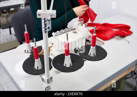 Young woman using professional overlock sewing machine in workshop studio. Equipment for edging, hemming or seaming clothes at t Stock Photo