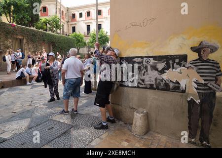 June 26, 2024, Malaga, Spain: A mural created by urban artist ''TVboy', that depicts the 'Guernica' painting of Spanish artist Pablo Picasso, is seen as tourists take photos on a street, amid a context of increasing rejection of mass tourism. Malaga has experienced significant growth in mass tourism and an increase in the number of tourist apartments in the city centre and neighborhoods. These factors have resulted in rising rental and housing prices. Local neighbourhood associations and organisations are calling for measures to be introduced to limit rental prices and the impact of mass touri Stock Photo