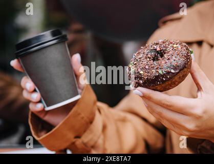 Female hands are holding a donut and a cup of coffee Stock Photo