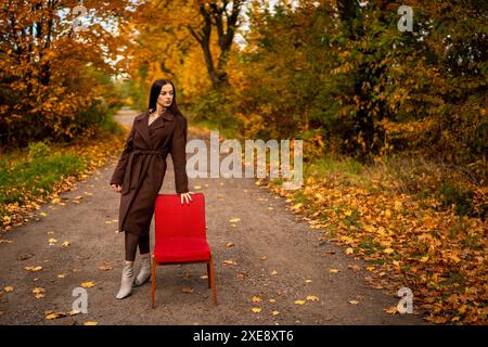 Portrait of a young woman with old armchair in a brown coat in autumn Stock Photo