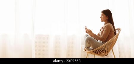 Woman Using Phone in Chair by Window Stock Photo