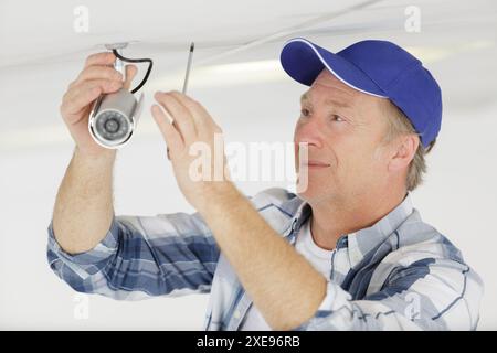 mature contractor installing cctv camera on ceiling Stock Photo