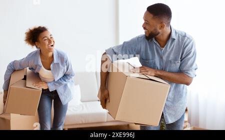 Joyful Afro Couple Carrying Moving Boxes Entering New Home Stock Photo