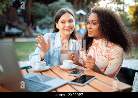 Two Women Using Laptop and Phone at Outdoor Cafe Stock Photo