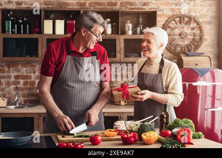 Senior Couple Cooking Together in Home Kitchen While Exchanging Gifts Stock Photo