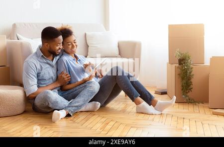Spouses Using Tablet Sitting On Floor Among Unpacked Boxes Indoor Stock Photo