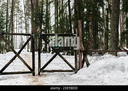 Old wooden gate entangled with iron barbed wire. Against the backdrop of a winter forest. Stock Photo