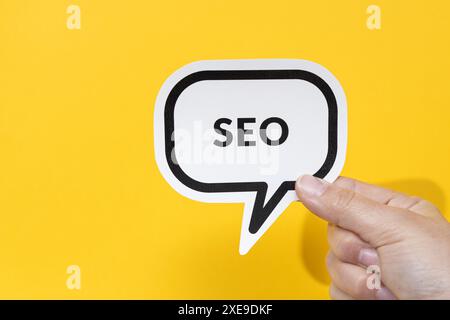 Hand holding speech bubble with text SEO isolated on yellow background Stock Photo