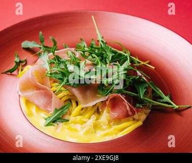 Spaghetti with prosciutto and arugula on red plate Stock Photo