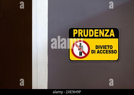 Black and yellow caution sign on the side of an open door stating  in Italian "Prudenza, Divieto di accesso", meaning "Caution, Access denied". Stock Photo