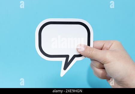 Hand holding a blank speech bubble isolated on blue background. Template Mockup Stock Photo