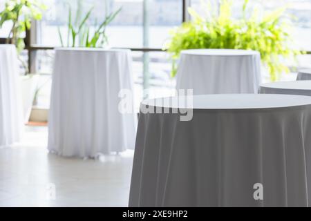 Round tables for the buffet are covered with white tablecloths, background photo Stock Photo