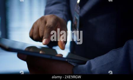 Technician in server hub checking recovery plan on tablet, monitoring energy consumption across mainframes. Close up shot of man in data center making sure rigs are functioning optimally, camera B Stock Photo