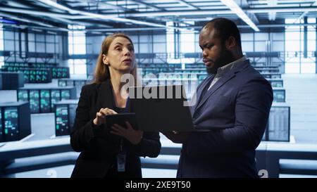 Manager in data center supervising worker running error checking utilities to fix errors. Supervisor in server farm overseeing engineer repairing network issues affecting rigs performance, camera A Stock Photo