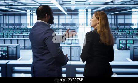 Data center engineer presenting equipment to inspector supervising operations. IT specialist in server farm doing tour for supervisor monitoring equipment performance, camera A Stock Photo