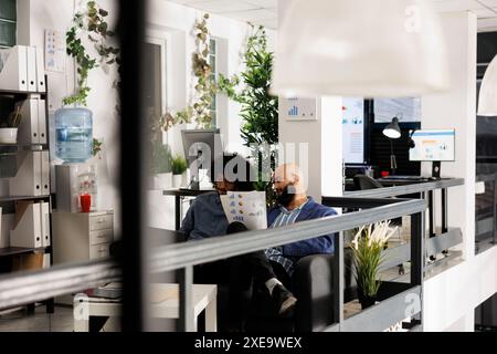 Two corporate employees discussing financial analysis and planning presentation in coworking space. Arab company analysts working in office, holding papers with charts and graphs Stock Photo