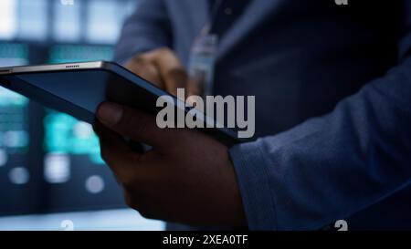 Software developer doing yearly maintenance using tablet to prolong data center equipment life span. Extreme close up of worker in server hub monitoring server infrastructure using device, camera B Stock Photo
