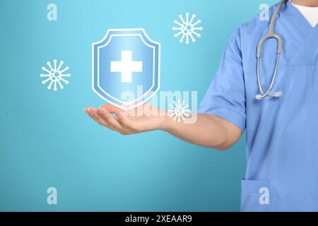Strong immunity blocking viruses. Doctor holding illustration of shield on light blue background, closeup Stock Photo