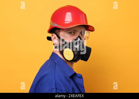 Man in respirator mask and hard hat on yellow background Stock Photo