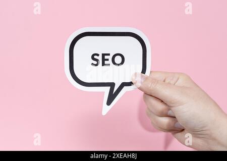 Hand holding speech bubble with text SEO isolated on pink background Stock Photo