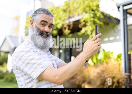 Taking selfie, senior man smiling and holding smartphone outside Stock Photo