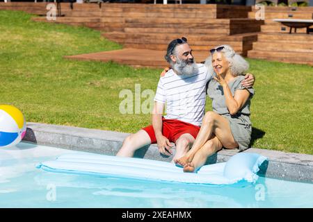 Senior couple sitting by pool, relaxing and enjoying sunny day together Stock Photo