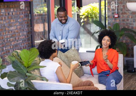 Diverse group of business colleagues discussing work, holding coffee cups in office Stock Photo