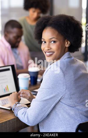 Smiling businesswoman using laptop with colleagues working in background at office Stock Photo