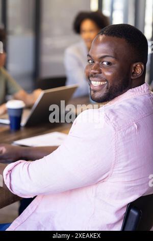 Smiling businessman in casual attire sitting at meeting table with colleagues Stock Photo