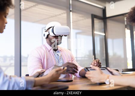 Using VR headset, African American businessman with colleagues and tablets in office meeting Stock Photo