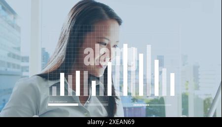 Image of graphs and loading bars, asian woman standing and using laptop in office Stock Photo