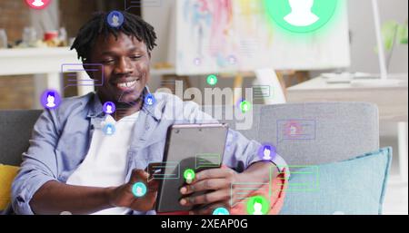 Image of media icons over happy african american man using tablet Stock Photo
