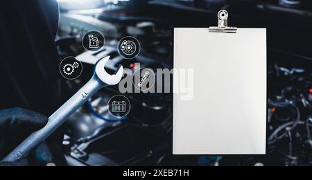 Car maintenance service concept , Blank white paper and mechanic hand holding a wrench for car repairing include an car engine blurred on background Stock Photo