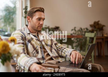 Lifestyle and workplace concept. Young handsome man in casual clothes, sitting in cafe with laptop, studying online, working rem Stock Photo