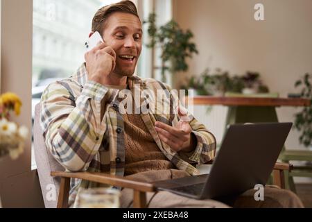 Handsome businessman in coffee shop, sitting in cafe with laptop and calling someone, Man talking on the phone with client, maki Stock Photo