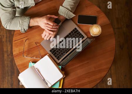 Top view of male hands, man checking time or message on his digital watch, sitting in a cafe with laptop, mobile phone and noteb Stock Photo