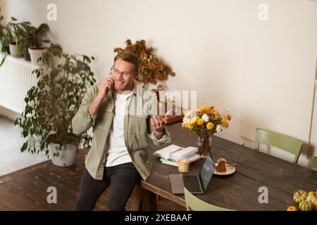 Portrait of happy young manager, man having negotiations, business conversation over the phone, talking on mobile, sitting in of Stock Photo
