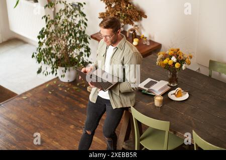 Image of young man, successful businessman sitting on table, looking at laptop, working in an office, looking concentrated on th Stock Photo