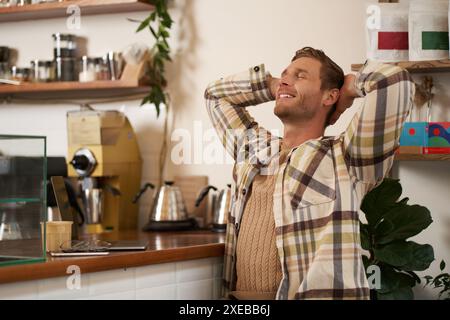 Portrait of man doing big stretch with satisfied smile, finishing his project, sitting in cafe with laptop and phone, drinking c Stock Photo