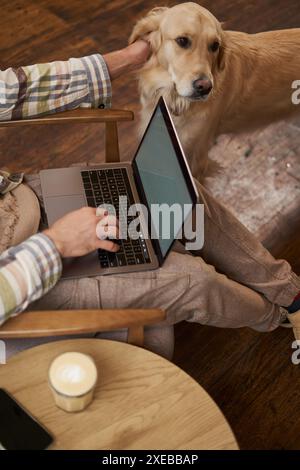 Vertical cropped picture of male hands typing on keyboard, using laptop and petting the dog, cafe visitor working and spending t Stock Photo