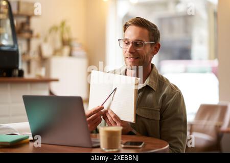 Portrait of young handsome man in glasses, private tutor teaching student online, pointing at his notebook, showing something, v Stock Photo
