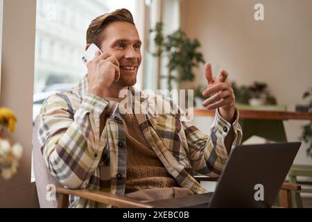 Handsome businessman in coffee shop, sitting in cafe with laptop and calling someone, Man talking on the phone with client, maki Stock Photo
