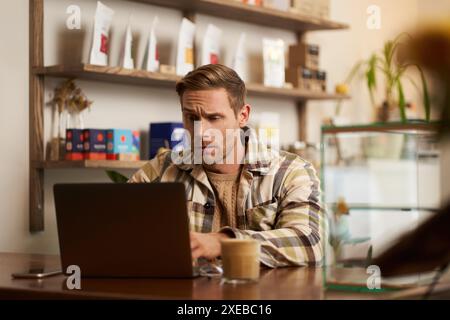 Image of young business owner, man sitting in cafe with laptop, looking confused at screen, digital nomad trying to solve the ta Stock Photo