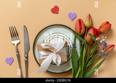 Beautiful table setting with  gift box, decorative hearts and tulips flowers on pastel peach background. Stock Photo