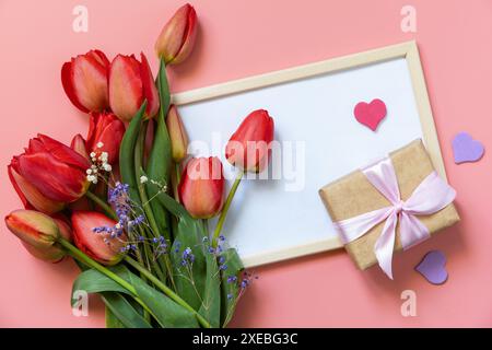Red tulips with gift box and small hearts on pastel pink background with empty space. Stock Photo