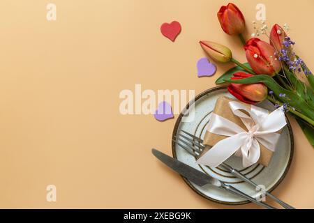Beautiful table setting with  gift box, decorative hearts and tulips flowers on pastel peach background. Stock Photo
