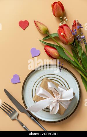 Beautiful table setting with  gift box, decorative hearts and tulips flowers on pastel peach background. Stock Photo