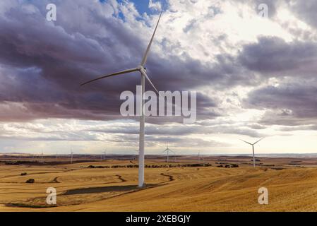 Dramatic sky over wind turbines in a vast, hilly agricultural landscape illustrating renewable energy Stock Photo