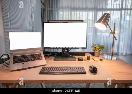 Set of computer device with blank monitor, laptop, table lamp, keyboard, mouse on wooden desk in minimal home office Stock Photo