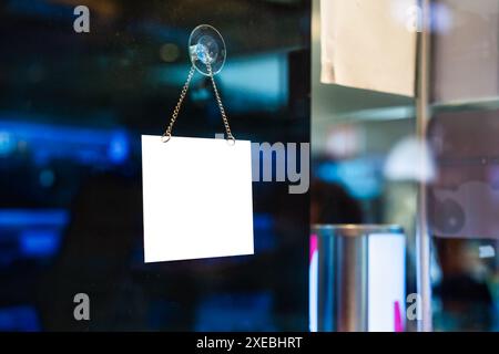 Empty white plastic signboard hanging on glass window in shopping store Stock Photo